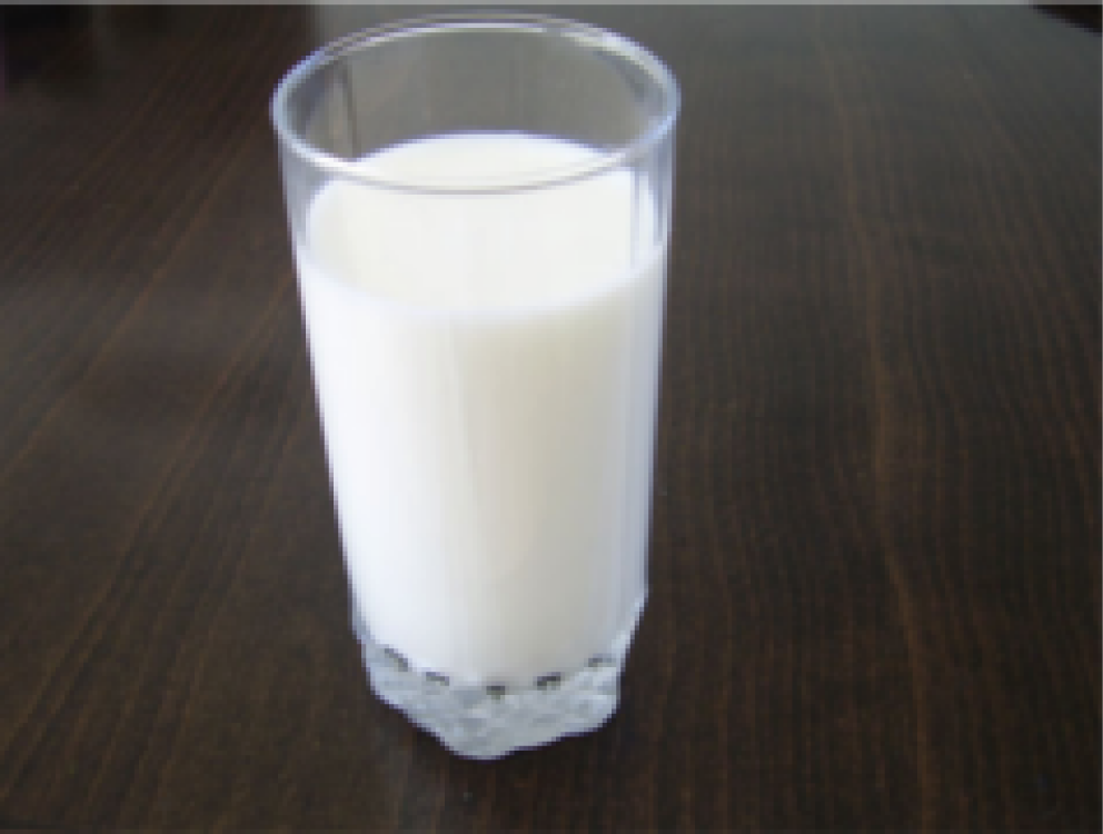 Ein Glas mit frischer, weißer Milch auf einem Holztisch.