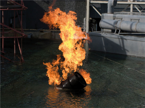 Ein brennendes Fass in Wasser mit Flammen, die nach oben schlagen.