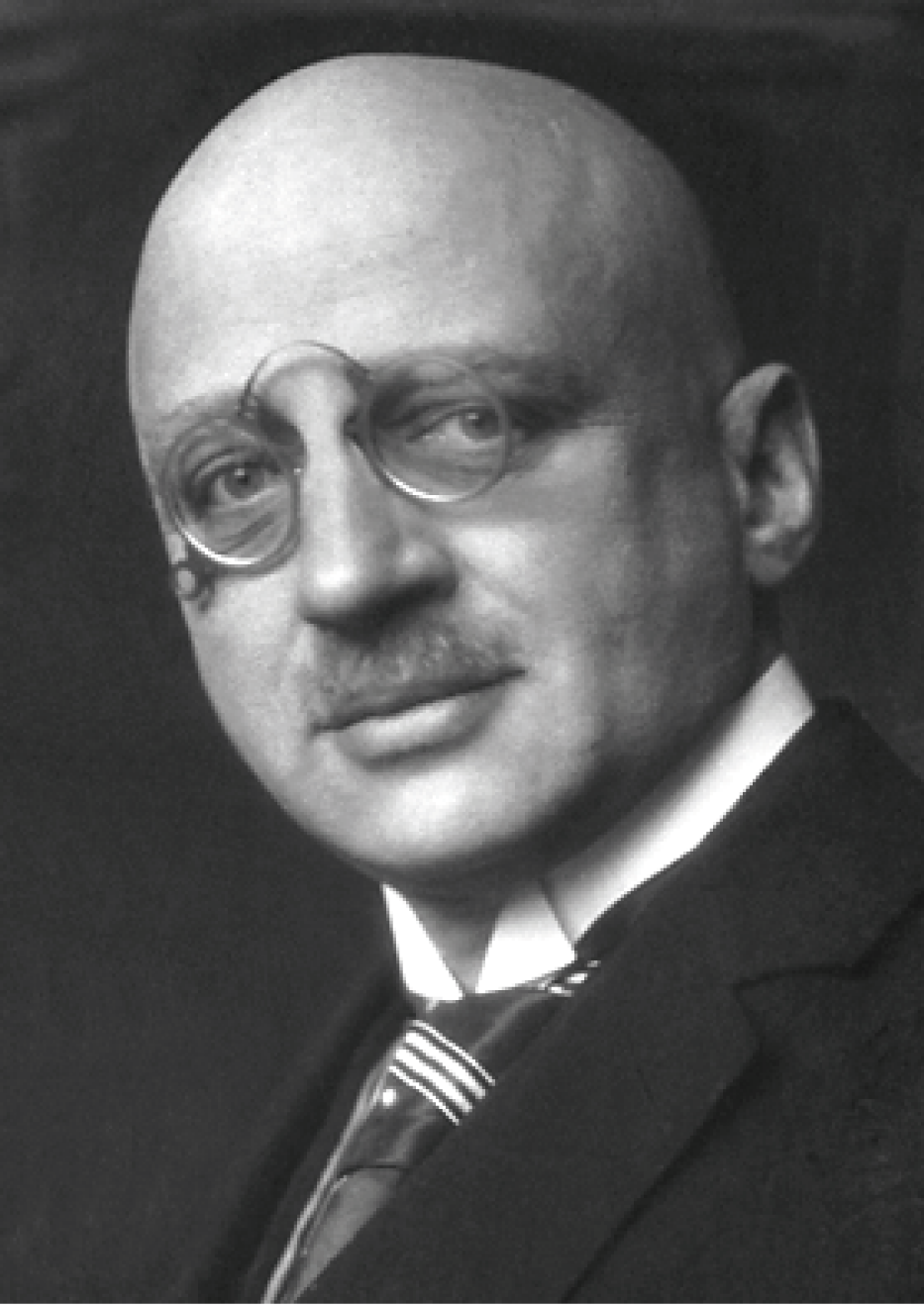 Porträt eines Mannes mit Glatze und Brille, der einen Anzug trägt und ernst schaut. Schwarz-weiß Fotografie.