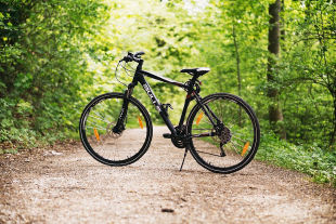 Schwarzes Fahrrad auf einem schottrigen Weg umgeben von grüner Natur.