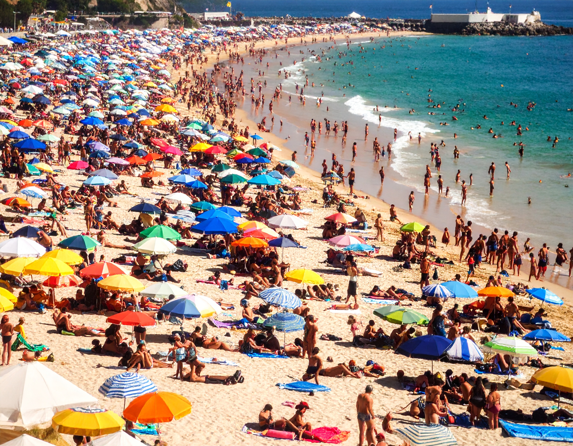 Blick auf einen belebten Strand mit vielen Sonnenschirmen und Badegästen, die sich am Wasser entspannen.