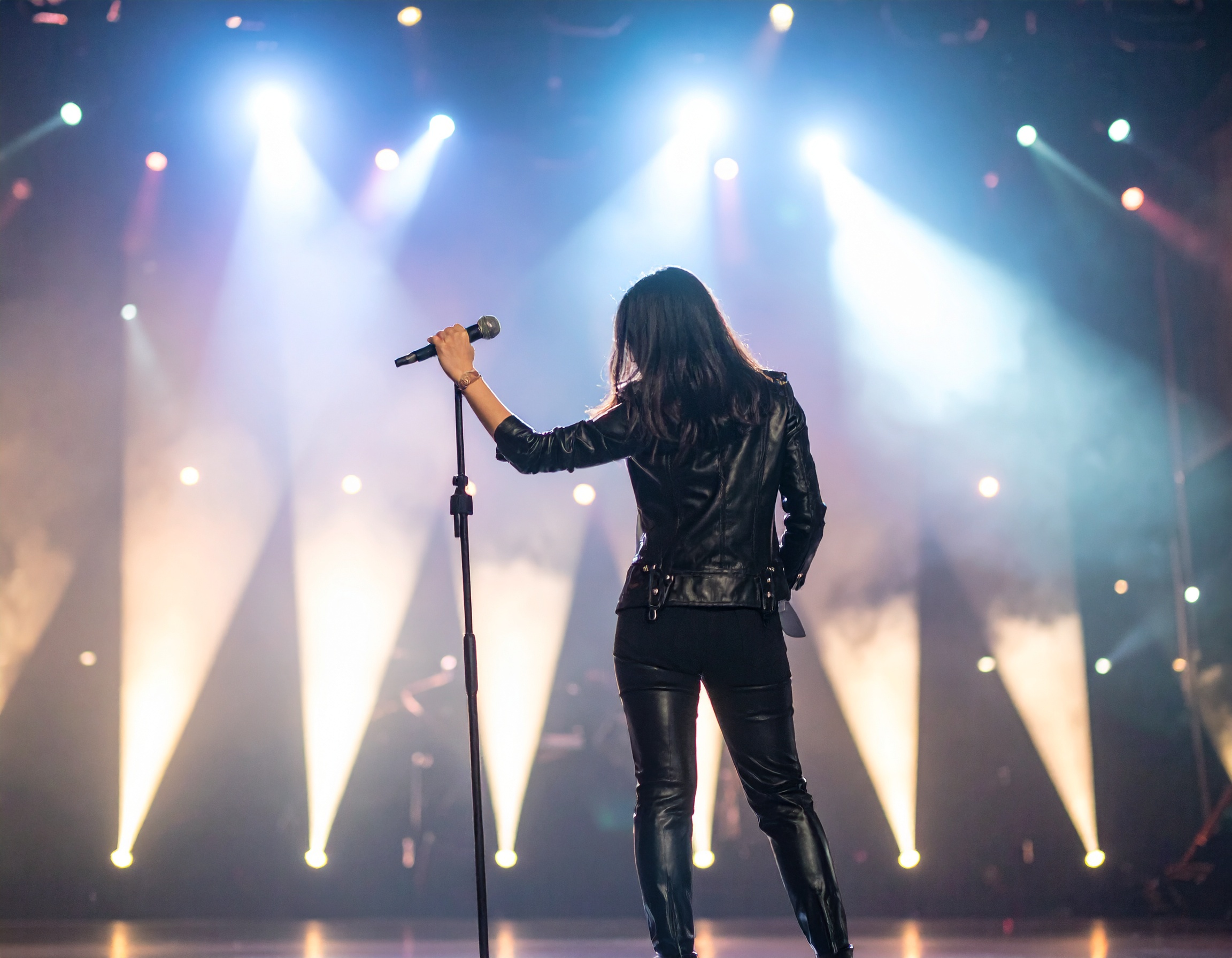 Sängerin auf der Bühne mit Mikrofon, beleuchtet von bunten Lichtern.