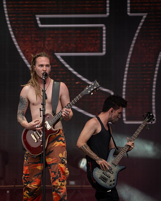 Zwei Musiker auf Bühne, einer mit E-Gitarre und Dreadlocks singt, anderer spielt Bass