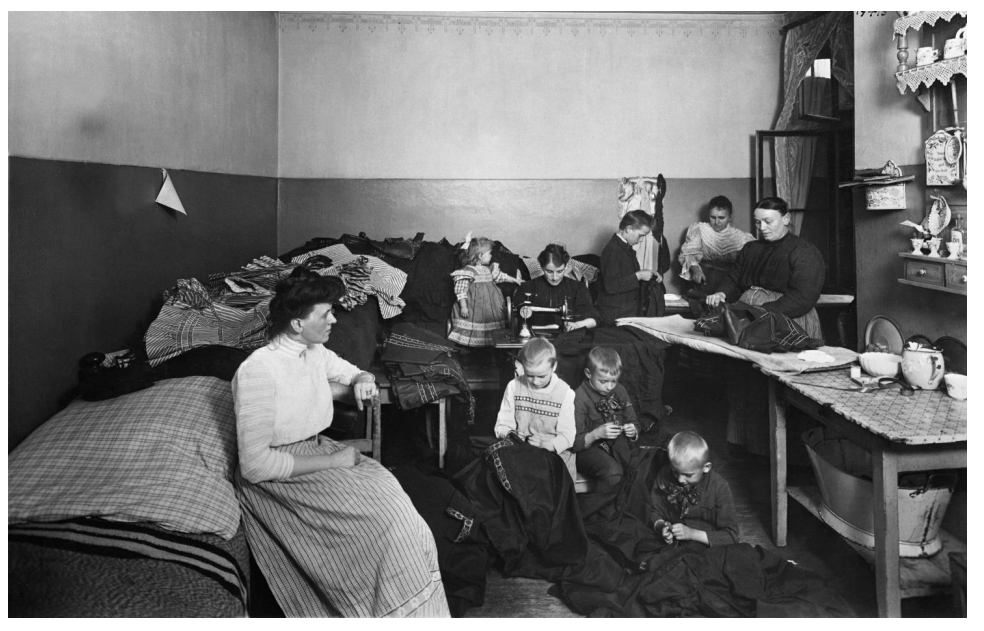 Schwarzweißfoto: Frauen und Kinder in einem Raum beim Nähen und Flicken von Kleidung.