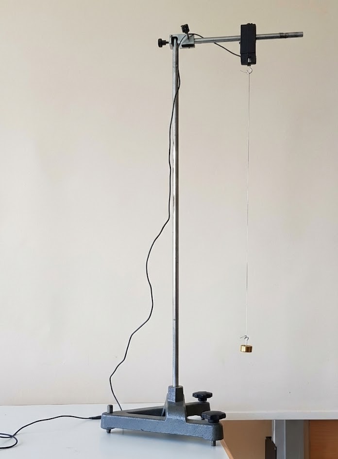 Metallstativ mit Klemme und herabhängender Messmasse an Faden auf Tisch