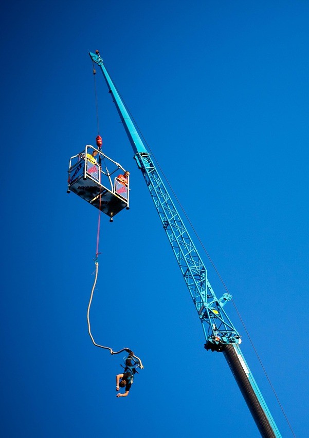 Person am Bungee-Seil springt von einer Kranplattform vor klarem blauem Himmel.