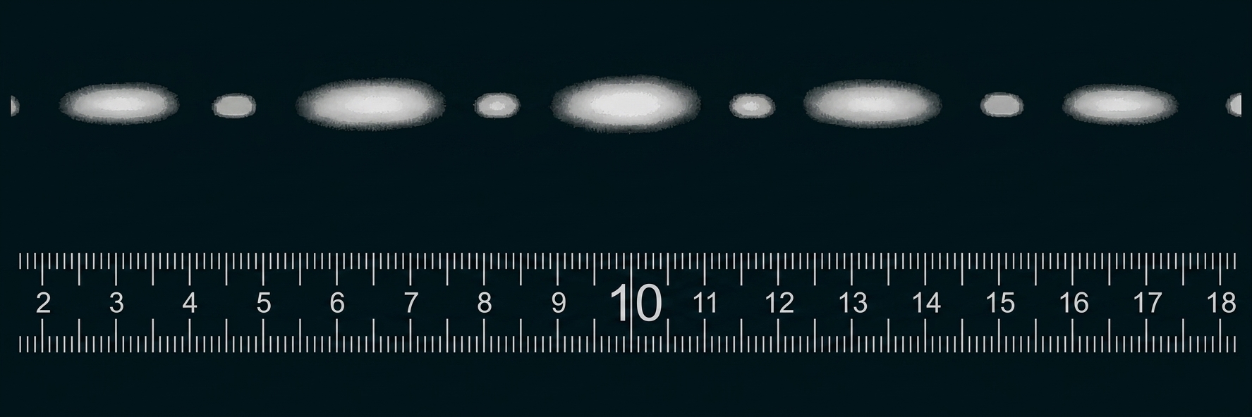 Lineal mit Zentimeter-Skala, darüber Reihe von grauen ovalen Flecken