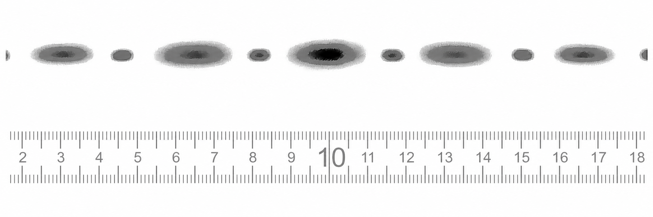 Lineal mit Zentimeter-Skala, darüber Reihe von grauen ovalen Flecken