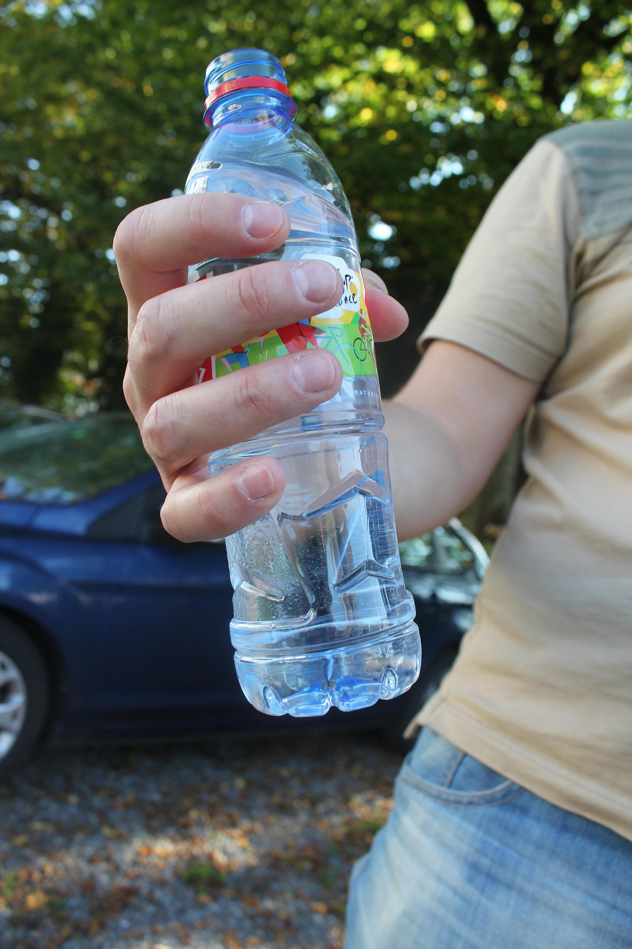 Hand hält eine Plastik-Wasserflasche im Freien.