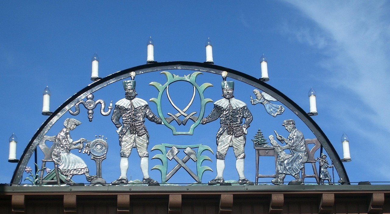 Dekorativer Metallbogen mit zwei Bergmännern, Frauen, Werkzeugen und Kerzen vor blauem Himmel