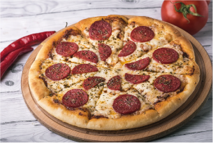 Pizza mit Salamischeiben auf einem Holzbrett, umgeben von Tomate und Chilischoten.