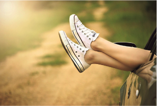 Füße in weißen Sneakers, die aus einem Autofenster hängen, vor einer unscharfen Landschaft.