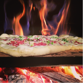 Pizza wird in einem Holzofen mit Flammen gebacken.