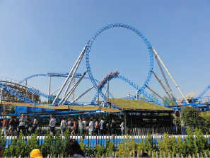 Eine Achterbahn mit blauen Schienen und vielen Besuchern an einem sonnigen Tag.
