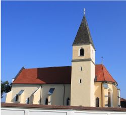Eine gelbe Kirche mit spitzem Turm vor blauem Himmel.